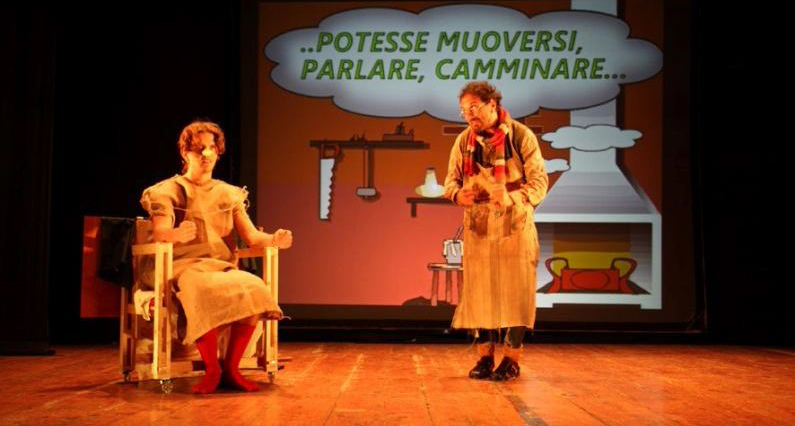 Una foto dello spettacolo accessibile "Le avventure del Piccolo Burattino" a cura dell'Associazione Li.Fra. Sulla scena Pinocchio e Geppetto e sul retro, la frase, che rappresenta il pensiero di Geppetto, "Potesse muoversi, parlare, camminare..."